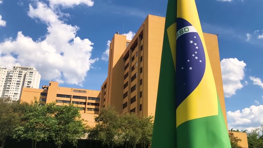 Brazilian Flag Slow Motion Waving at Park with Buildings Behing and Blue Sky