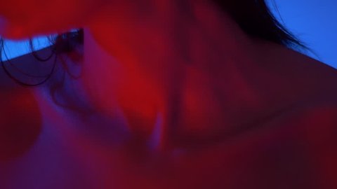 Close-up shot of collarbone and chin of futuristic and sexy fashion model in bright red neon lights in studio.