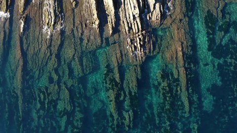 Aerial top-down view over coastal rocks and transparent-turquoise sea
