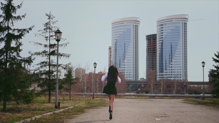 Happy asian girl jumping on road in short school uniform. Model turns and smiles. Student straightens her hair in a jump, it looks very cute. Person rides very pretty on the background of skyscrapers.
