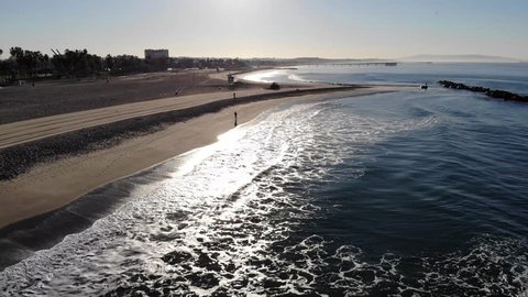 Aerial footage of a city beach in the morning. Flying over jogger, lifeguard tower, Pacific Ocean