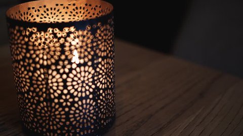 A burning candle inside a holder with a pattern, an old bar with candles burning set the atmosphere, 4k footage
