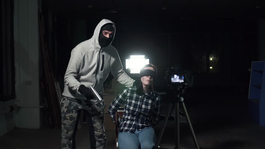 Kidnapper with a gun threatens a young woman bound blindfolded through