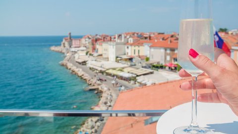 A young woman is standing on the balcony and is observing the streets of Piran. She is about to have a nice drink on this great summer day.