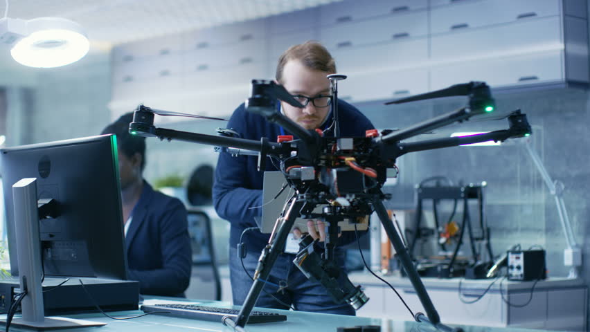 Handsome Man and African American Woman Engineers Working on a Drone Project with Help of Laptop and Taking Notes. He Works in a Bright Modern High-Tech Laboratory. Royalty-Free Stock Footage #1027774661