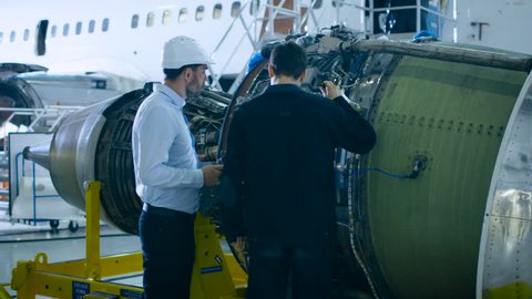 Aircraft Maintenance Mechanic and Chief Engineer Uses Digital Tablet Computer to Analyze, Inspect and Work on Airplane Jet Engine in Hangar. Optimal Functionality, Work, Efficiency and Safety