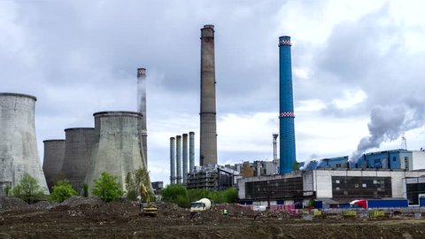 Time lapse of thermal power station with cooling towers emitting smoke, while a few concrete mixer trucks work in the front. Storm clouds moving in. Industrial, energy generation, coal burning.