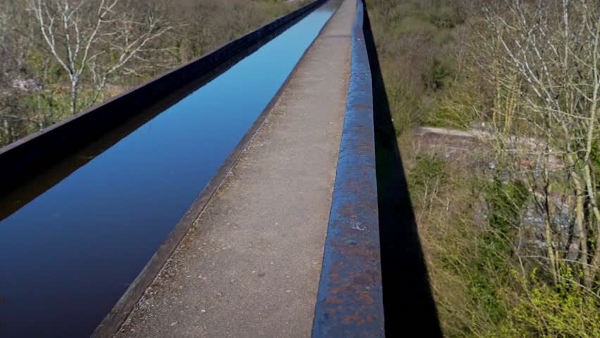 An elderly couple with grey hair walk across the famous Pontcysyllte Aqueduct on the Llangollen canal route in the beautiful Welsh countryside