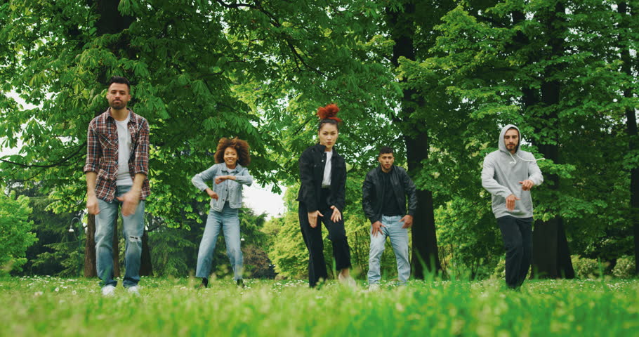 Slow motion of group of young urban dancers of different ethnicities are having fun to training in a green city park on a sunny day.