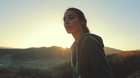 pretty woman hiker sits on edge of cliff against background of sunrise