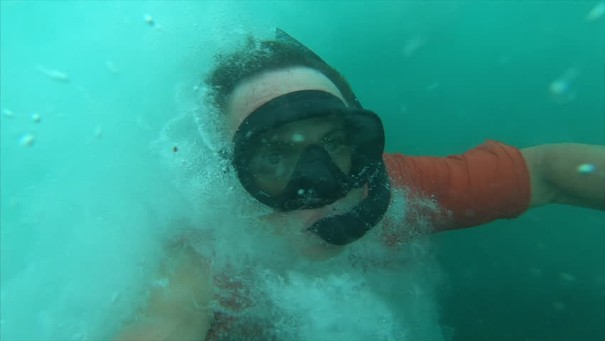 Underwater view of the young man swimming under the breaking wave and moving against the powerfull streams