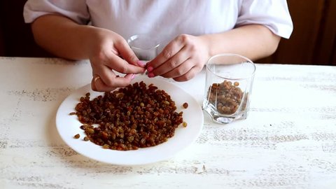 Young housewife cleans raisins from the tails on a white plate on a light wooden table in the kitchen. Women's hands. Healthy, natural food. Close-up.