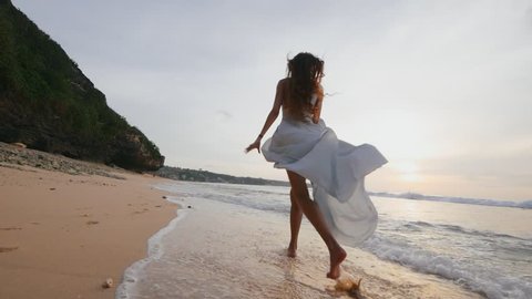 Slim beautiful young girl model in a waving long dress runs along the beach on a warm summer evening during the honeymoon