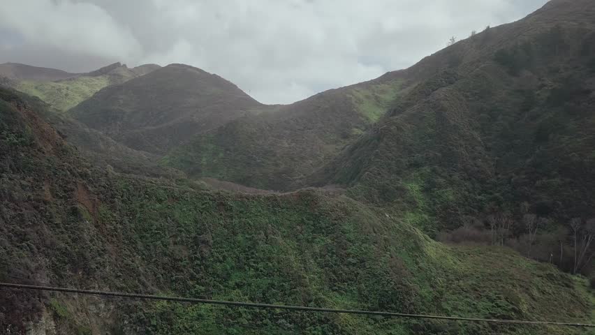 Pull back aerial drone view passing underneath close to South Pacific Highway as traffic passes overhead. Reveal view of full bridge & green mountain rocky valley.