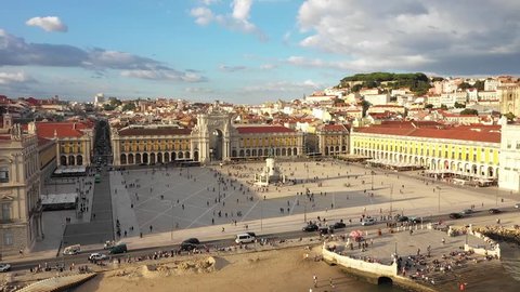 Aerial view of the Praca do Comercio in Lisbon, Portugal, during golden hour, with long shadows and the city in the background, including Castelo de Sao Jorge. Shot with a drone.