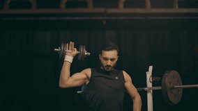 Muscular bearded sportsman training with dumbbell and looking away