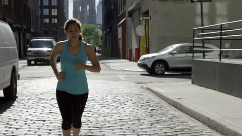 Woman Jogging on Cobblestone Street in BK with Brooklyn Bridge in Background - Female Athlete Running - Runner in Slow Motion 4K - Jogger Training in New York City - NYC, USA