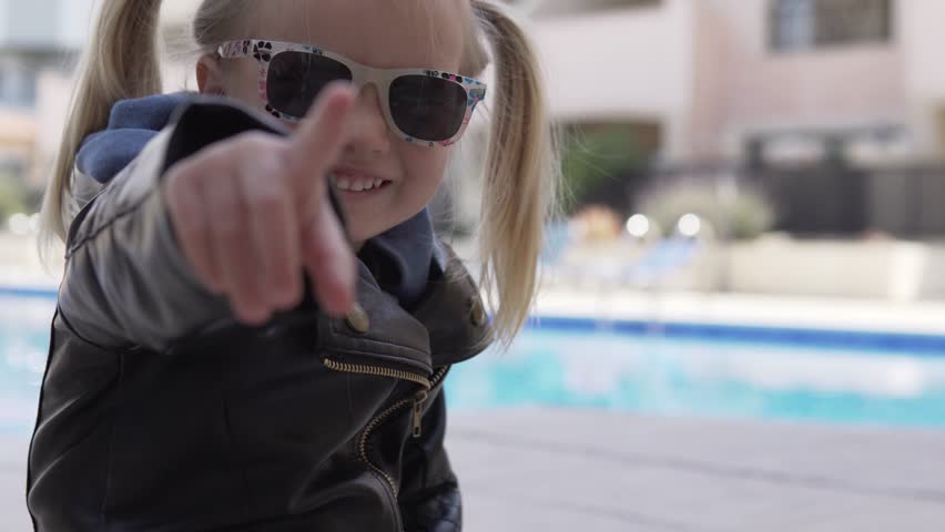 Fashionable little girl walks in the yard. She waves her hand at the camera.