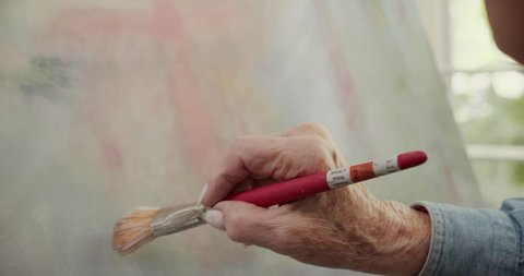 Senior citizen painting on canvas in slow motion close up on hands.