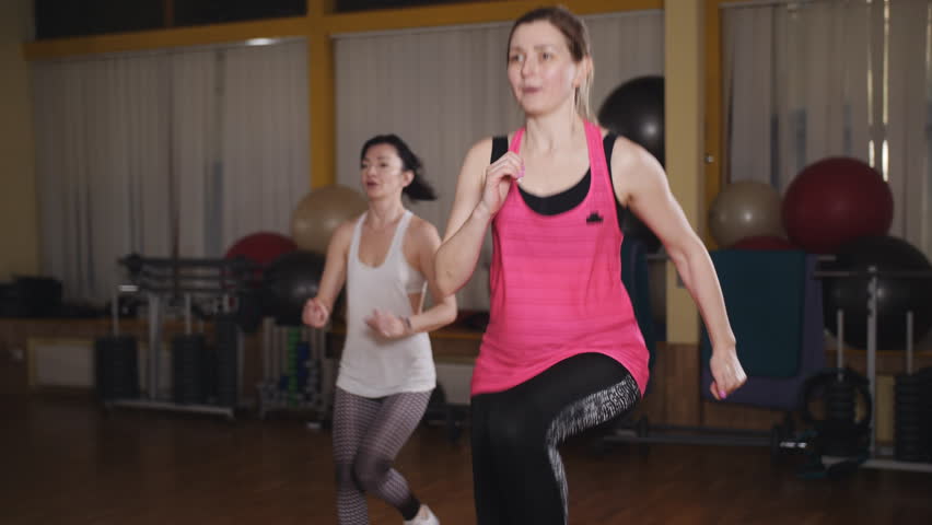 Two beautiful sports girls squats in the gym. Two girls doing step aerobics front lunge with dumbbells on platform