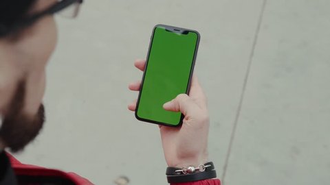 Los Angeles, California 15/03/2019 EDITORIAL: Back shot hands man stand holding and touching phone with green screen vertical background pavement digital internet modern screen smart phone technology