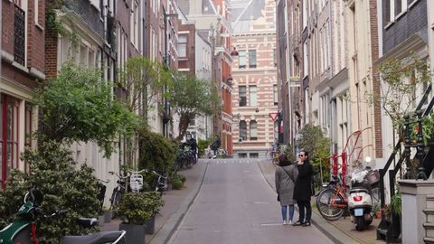 AMSTERDAM, NETHERLANDS - APR 13, 2019: Beautiful city streets and buildings architecture facades in center daytime people walk and ride bicycles