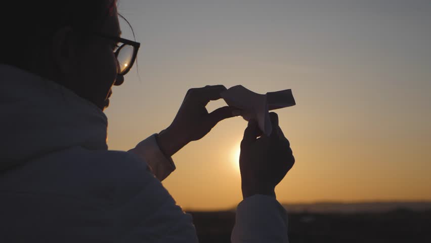 Silhouette of young girl throwing paper airplane at sunset.