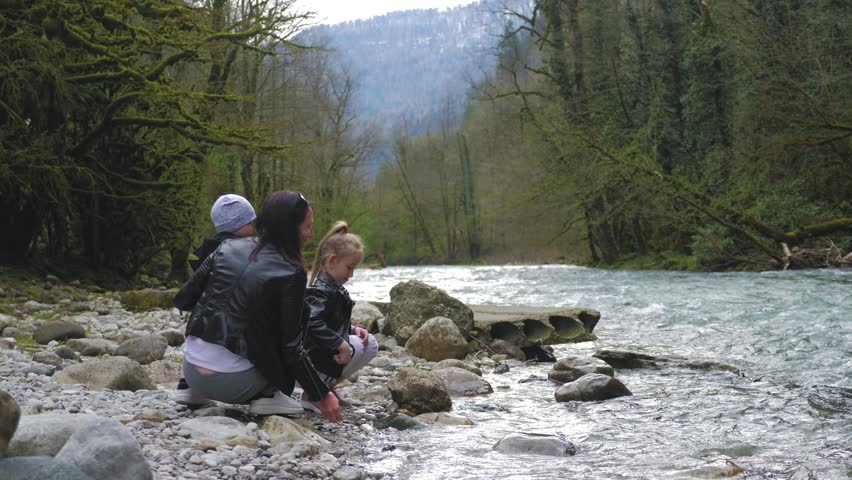 Mother with two toddler children outdoors playing by the mountain river.