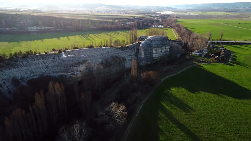 Top view of green fields and rock wall. Shot. Panoramic view of natural stone wall with trees on background of houses and mountain horizons on sunny summer day