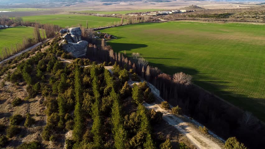 Top view of green fields and rock wall. Shot. Panoramic view of natural stone wall with trees on background of houses and mountain horizons on sunny summer day