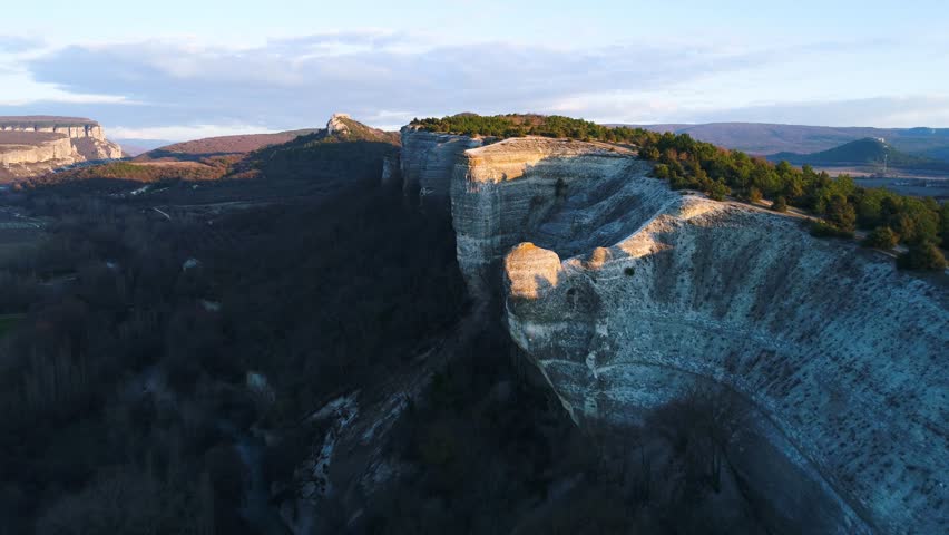 Top view of stone cliff with green bush at peak. Shot. Beautiful mountain landscape with rock casting shadow from evening sun and separating dark and light sides