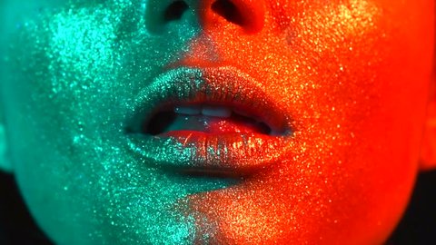 Fashion model woman licking lips in bright sparkles, colorful neon lights, beautiful sexy girl lips, mouth. Trendy glowing gold skin make-up. Art design makeup. Glitter metallic shine makeup 4K slowmo