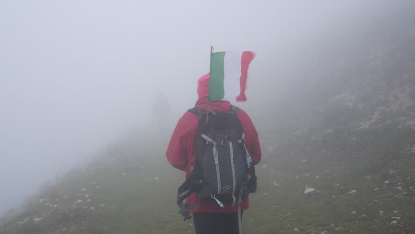 hiker on a mountain path in the fog with the Italian flag on the backpack. Taburno Regional Park, Montesarchio, Benevento, Italy