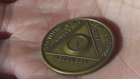 Hand opening and showing Alcoholics Anonymous medal with 5 years of sobriety