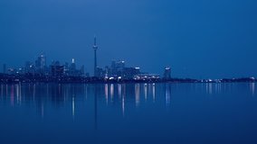 Video footage timelapse - sunset over Toronto City skyline in 4K. City buildings and skyscrapers get lit up with electric lights, colorful light reflection on water surface of lake Ontario.