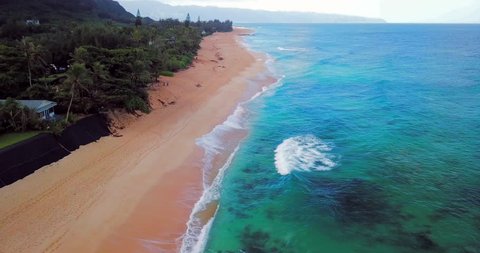 Aerial: Panning Above Ocean, Sandy Beach & Beachfront Buildings & Vegetation in Oahu, Hawaii