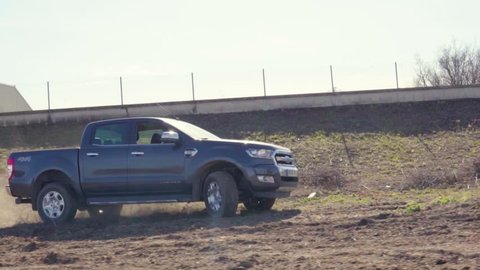 Barcelona / Spain - 11 02 2019: Slow motion footage of 4x4 pick up car drifting on a dusty field or driving off road while dirt scatters from under the wheels at the sunset.
