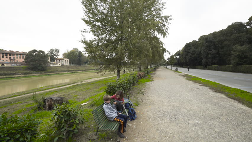 Two boys kidding around on park bench next to Arno River in Florence