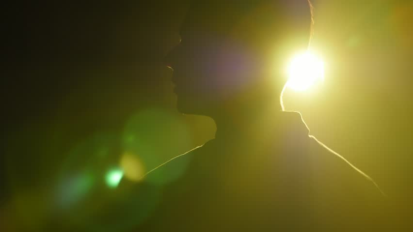 Silhouette of young man walking and looking around in the dark smoky room. Bright yellow lamp behing the man