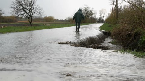 Disaster. Flooding in the village. Dirty black rivers flow along the road. A man in black rubber boots walks through the puddles.
