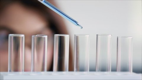 Slow motion scene video of  blurred at woman scientist dropping liquid into test tube in laboratory room.

