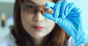 Zoom in scene video of blurred at female scientist that holding sample glass in her hand in laboratory room.
