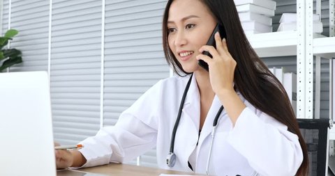 Good looking female doctor using notebook for check her patient illness history during talking to smartphone with him in hospital.
 Stockvideó