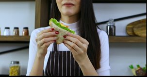 Zoom in scene video of Asian woman eating  sandwich in kitchen.
