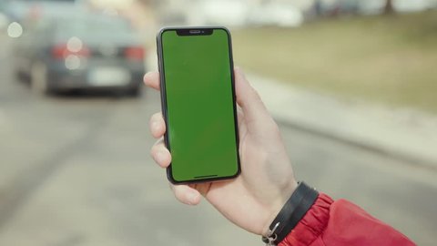 Los Angeles, California 15/03/2019 EDITORIAL: Hands man stand holding and touching phone with green screen vertical background road car city digital internet modern screen smart phone technology