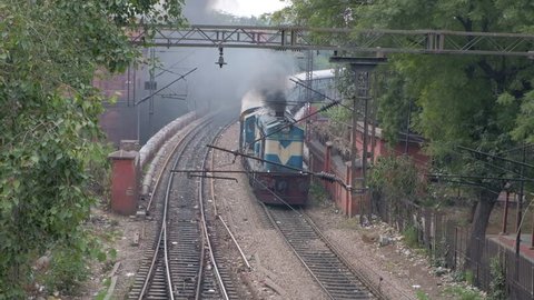 Delhi, india - 8 March 2019: Passenger train passing under a walkover bridge running on coal and emitting a great amount of dark black smoke as it creates pollution and reduces visibility 