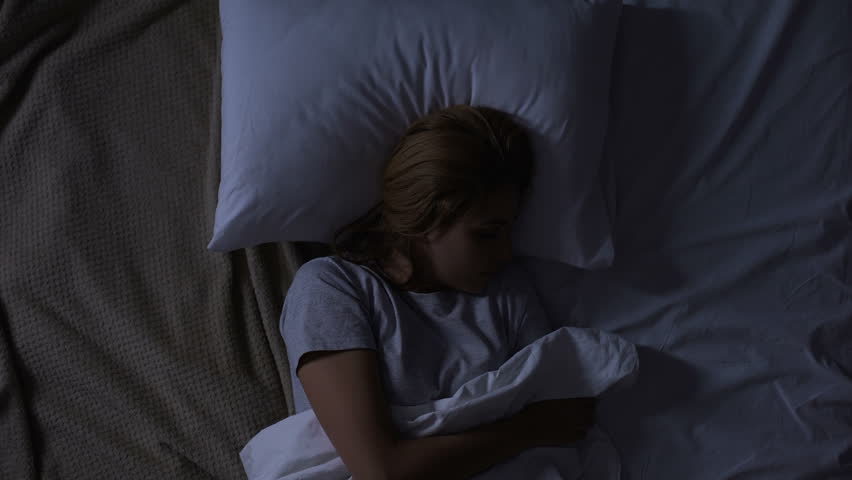 Pretty woman turning in her bed feeling discomfort, bad quality of mattress | Shutterstock HD Video #1027911944