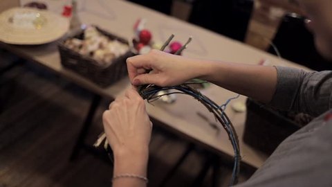 Close up of female hands tying up wooden rods with a flexible blue wire by a thin wire. Wooden base for christmas wreath. Handmade christmas decoration process at studio