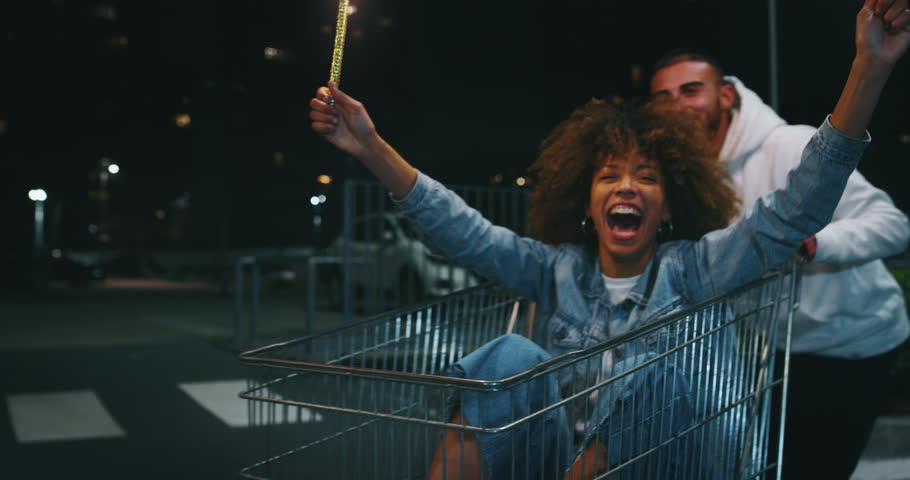 Slow motion close up of group of young friends of different ethnicities are having fun together racing on shopping carts and sparklers at supermarket parking at night. Royalty-Free Stock Footage #1027914608