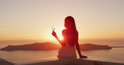 Woman at sunset. Luxury lifestyle - Woman drinking champagne. Elegant lady holding wine class looking at sunset over the ocean enjoying amazing view on luxury travel vacation. SLOW MOTION shot on RED.